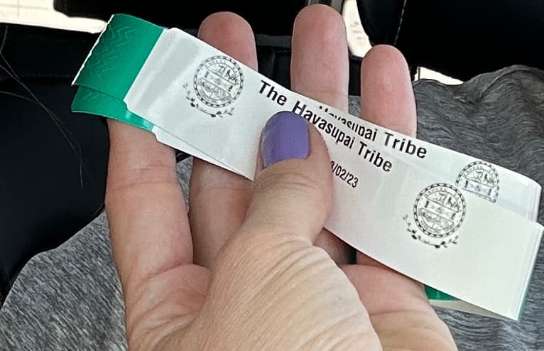 A close-up of a hand holding official Havasupai Tribe wristbands, required for accessing and camping at Havasu Falls, Arizona.