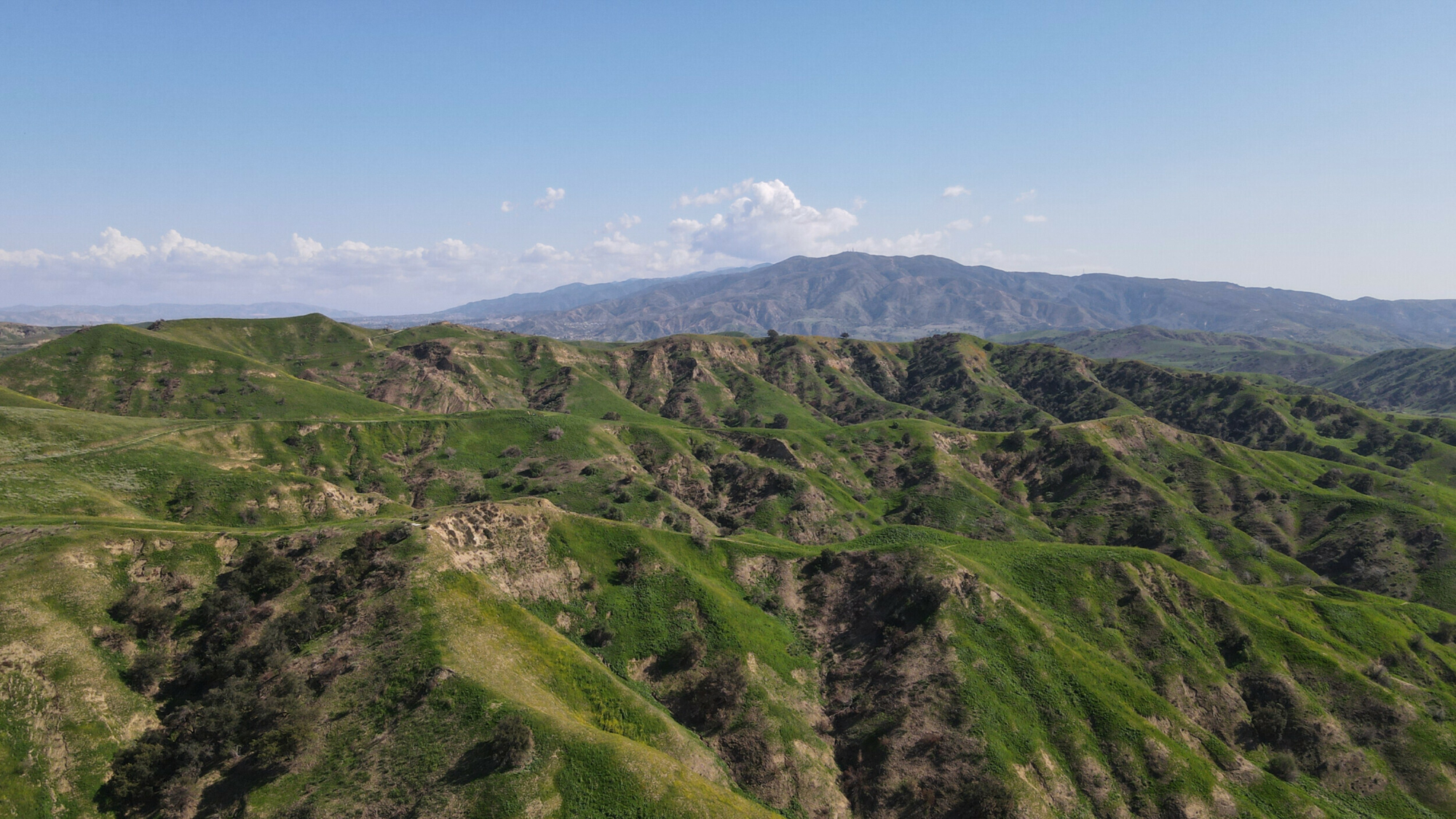 Aerial view of rolling green hills under a clear blue sky at Chino Hills State Park captured by DJI Mavic Air 2 drone.