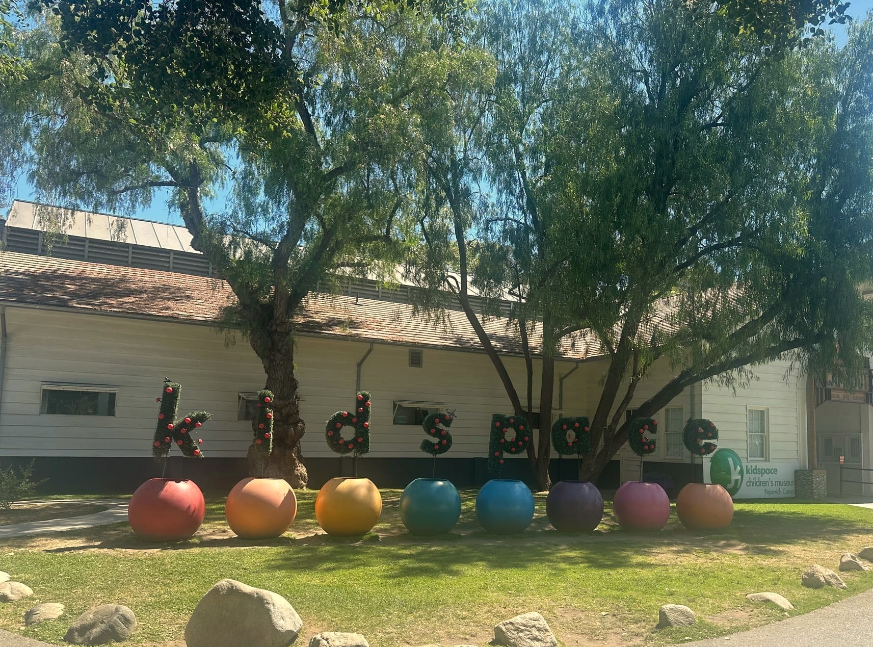 Entrance of Kidspace Children's Museum with colorful apple sculptures in front of a white building.