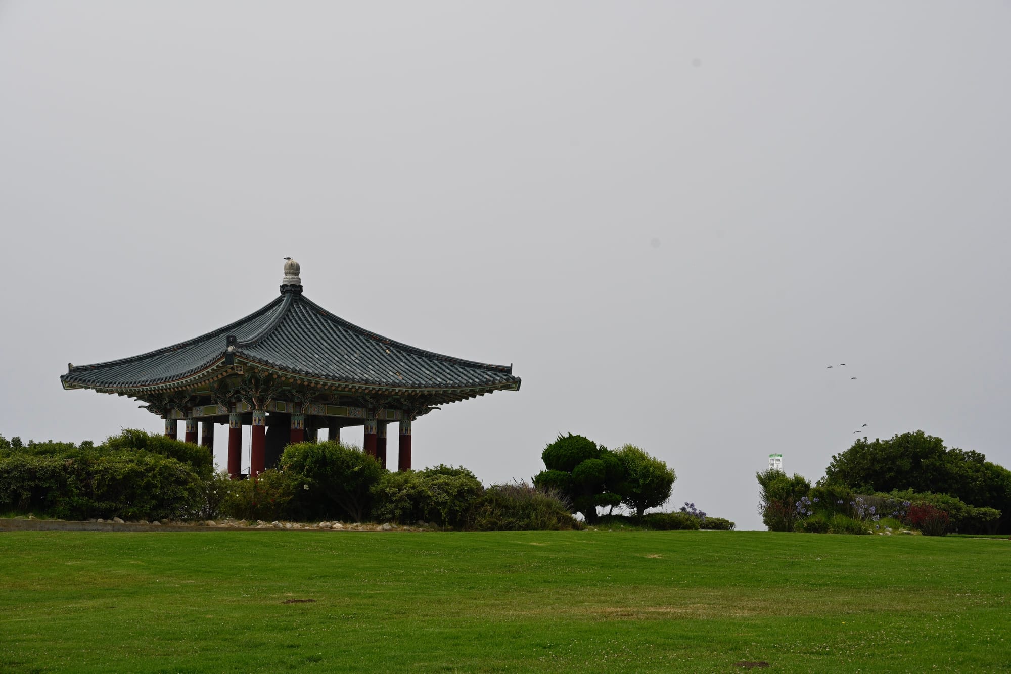 The Korean Bell of Friendship pavilion in San Pedro, set against a foggy sky with green lawns and bushes in the foreground.