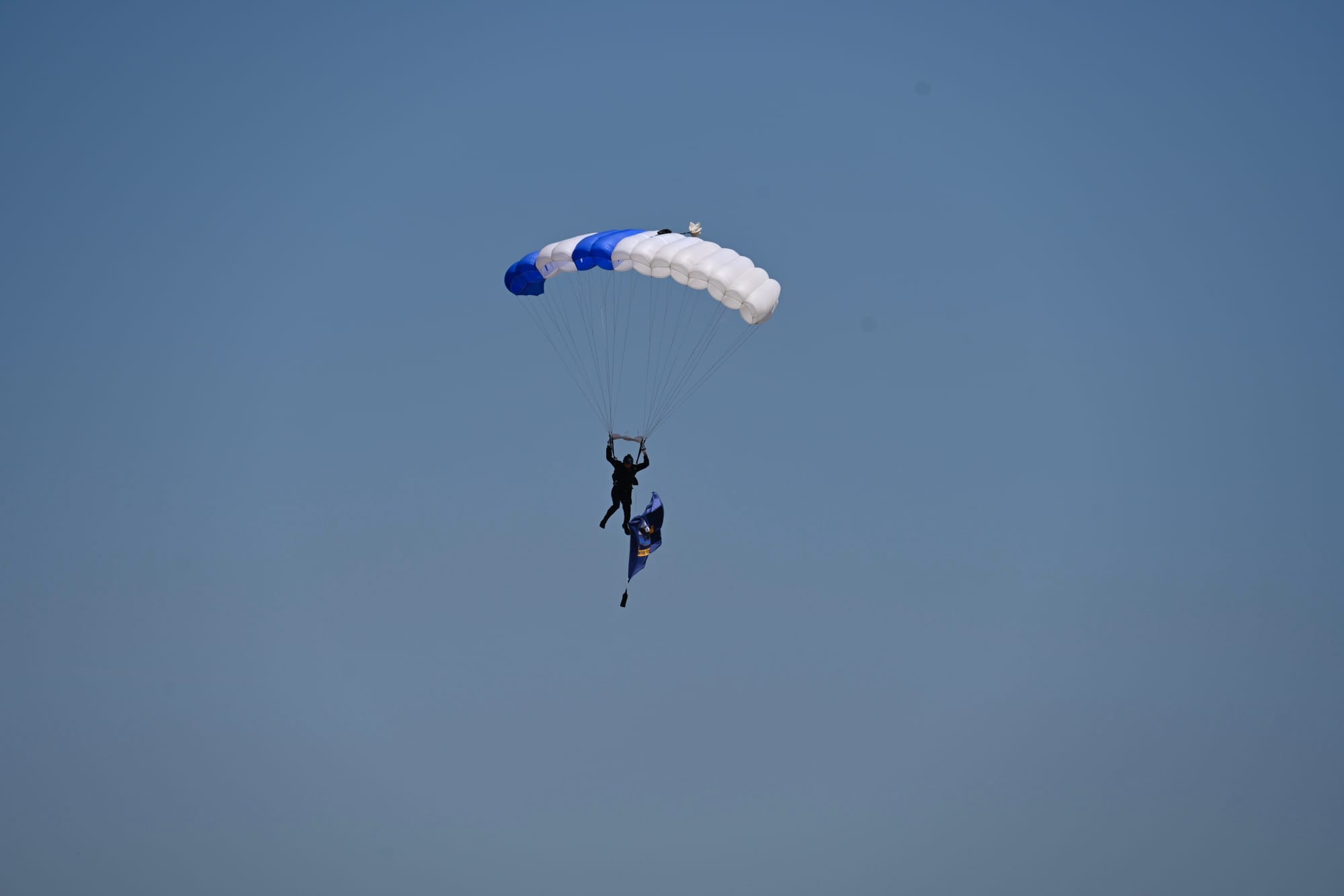 Parachutist descending while holding a flag against a clear blue sky during the Wings Over Camarillo Airshow.