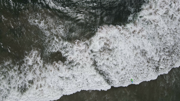 Aerial photograph of the frothy waves along Malibu's pristine coastline, with a lone figure standing on the shore