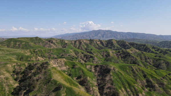 Aerial view of rolling green hills under a clear blue sky at Chino Hills State Park captured by DJI Mavic Air 2 drone.