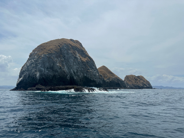 Rocky islands with grassy tops in the ocean near Tamarindo, Costa Rica, under a partly cloudy sky.