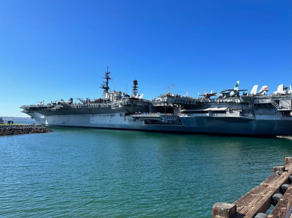 The USS Midway Museum, a large aircraft carrier docked in San Diego Harbor, under a blue sky with planes on its deck.