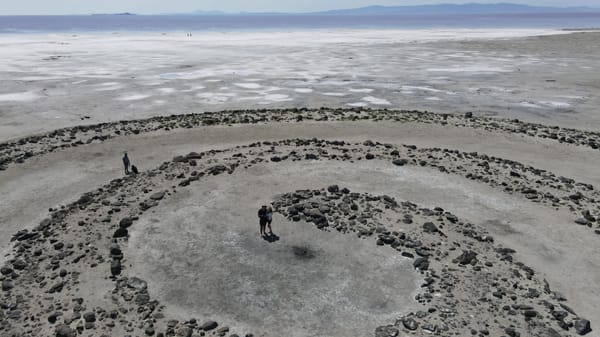 Visitors at the Spiral Jetty with salt flats and pink waters in the background.