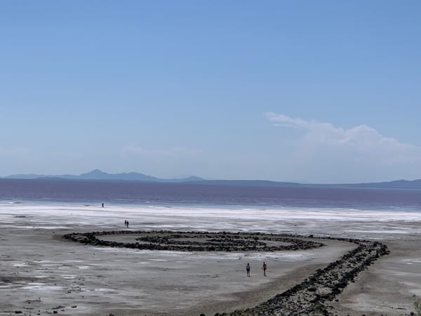 Visitors walk around the Spiral Jetty with the pink waters of the Great Salt Lake and distant mountains in the background.