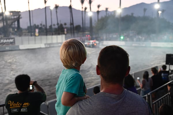 Father holding son as they watch cars drifting at Drift Night, Irwindale Speedway.