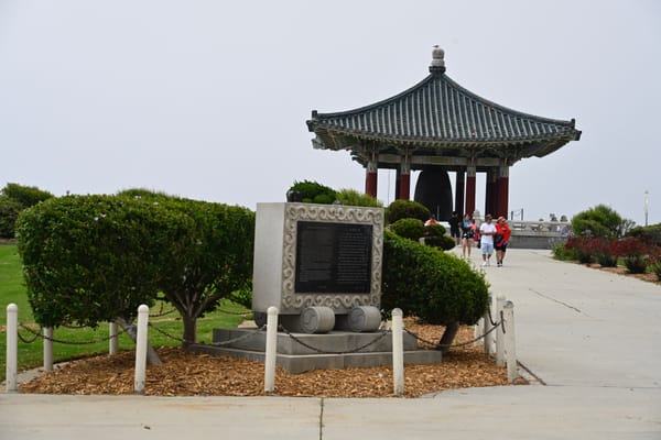 People walking to the Korean Bell of Friendship Pavilion in San Pedro, with a commemorative plaque visible in the foreground.