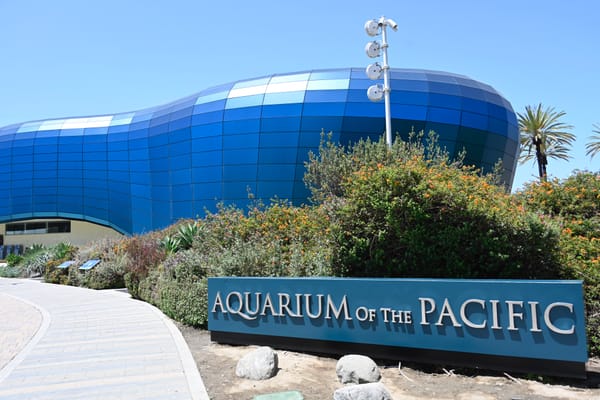 Exterior view of the Aquarium of the Pacific in Long Beach, featuring a modern, wave-like blue facade and lush landscaping.