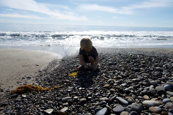 A young child crouching on a rocky Malibu beach with ocean waves in the background.