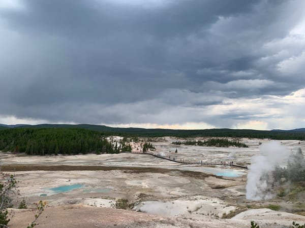 Storm clouds loom over Yellowstone's geyser basin, contrasting the vibrant geothermal features with the darkening sky.