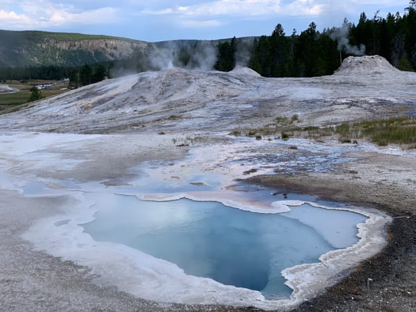 Geothermal area in Yellowstone National Park. Steaming geysers and a hot spring surrounded by a rocky terrain and hills.