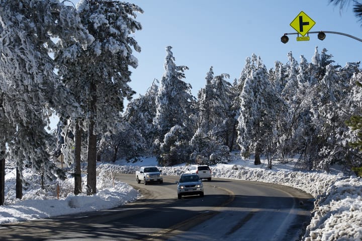 A group of cars driving down a snow-covered mountain road with snow-covered trees on the sides.